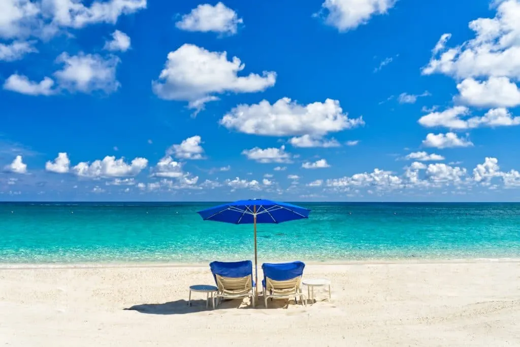 Beach chairs and a blue umbrella on a pristine Bahamas beach.